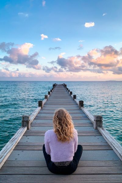 Photo d'un ponton donnant sur l'océan avec une femme aux cheveux longs blonds assise de dos en tailleur Accueil du site Xavier Magnétiseur Energéticien